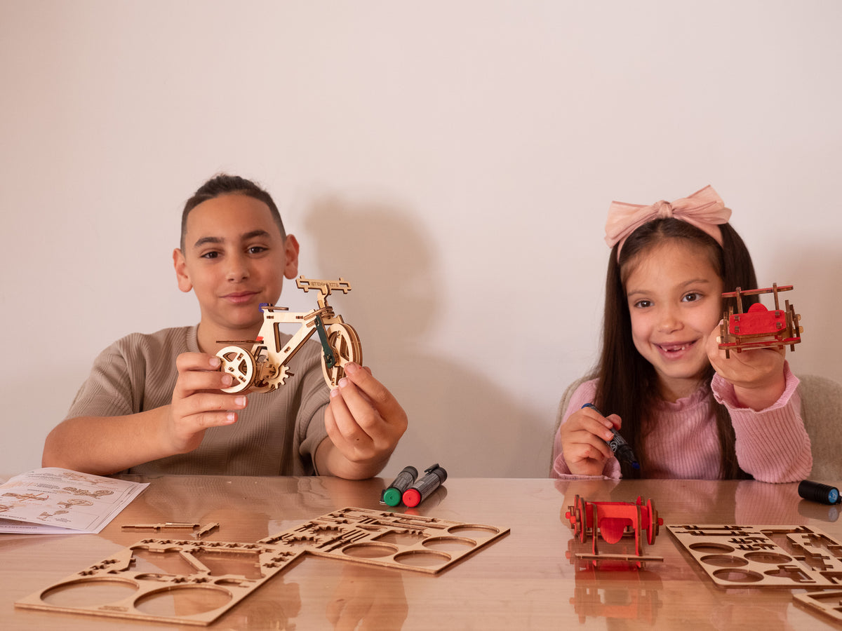 Two kids proudly holding their finished wooden Trike and coloured Race Car builds